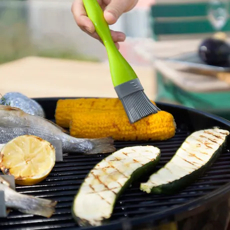 Person bestreicht Mais mit dem Silikonpinsel von Outdoorchef in Grün. Person bestreicht Mais mit dem Silikonpinsel von Outdoorchef in Grün.