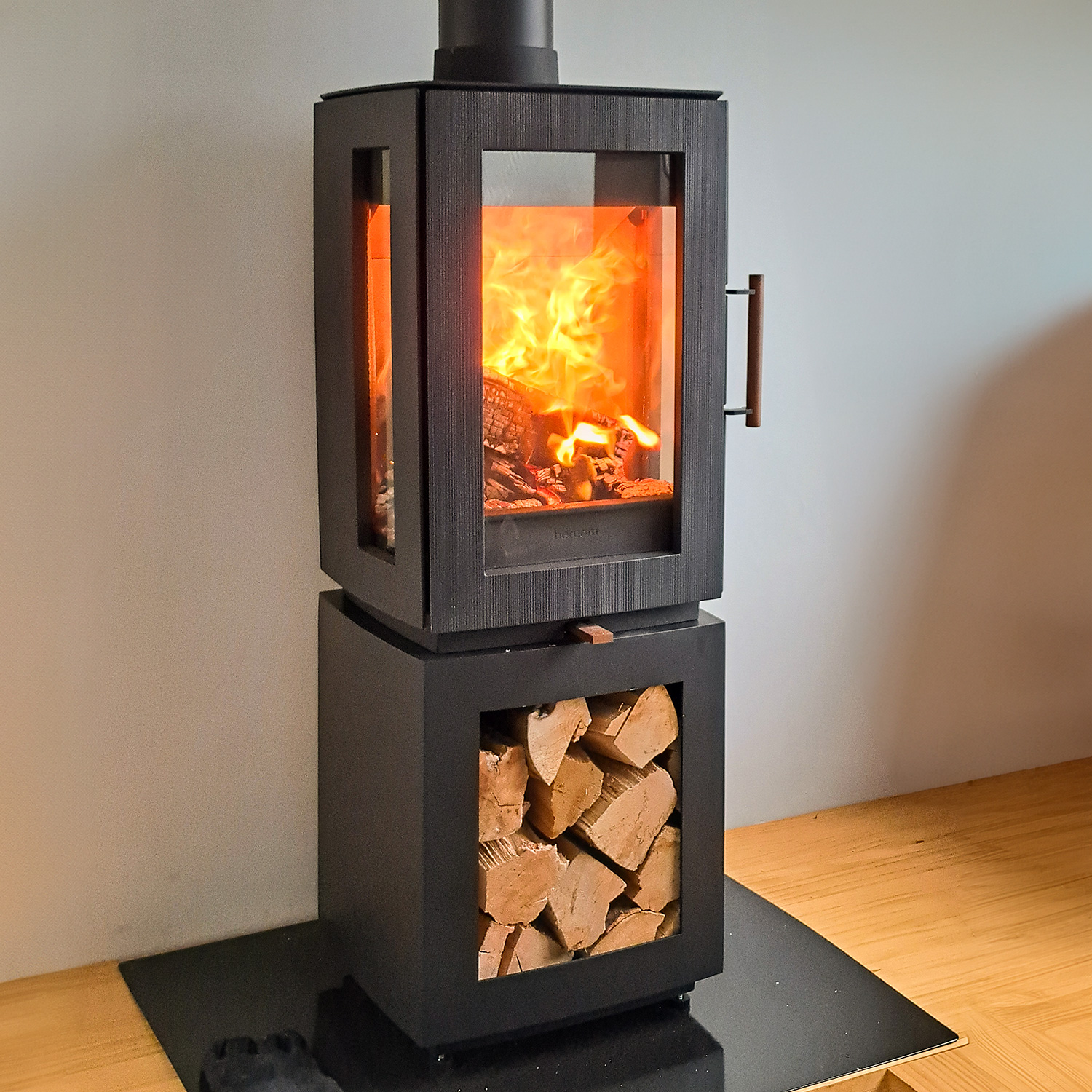 Poêle à bois Hergom Glow en fonte noire avec compartiment de rangement pour le bois