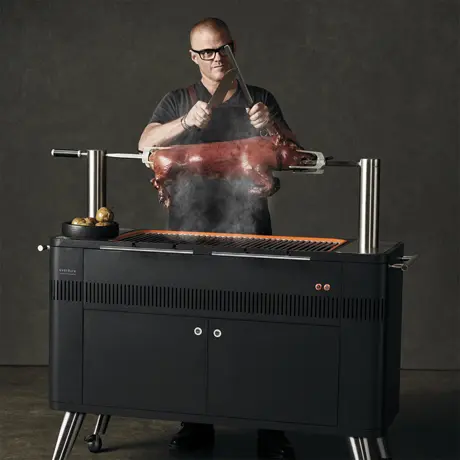 Mann grillt ein ganzes Schwein auf einem Everdure HUB Holzkohlegrill mit Spieß